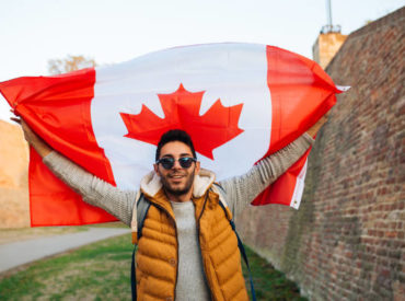 Young handsome man waving Canadian flag outside in the park